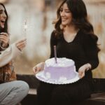 two lovely women sitting outdoors with birthday cake and sparkler