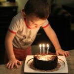 boy in crew neck t shirt looking at the chocolate cake with candles
